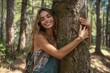 © Pinklife - A radiant woman embraces nature, her long hair cascading over the tree's trunk, as she poses with a genuine smile in a serene woodland setting during a photo shoot
