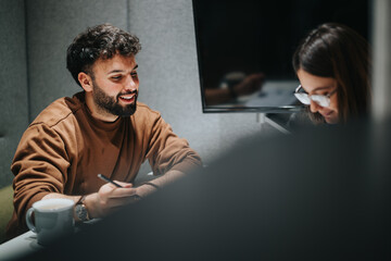 Wall Mural - A cheerful young male professional engages with a focused female coworker at a well-lit contemporary workspace, indicative of teamwork and productivity.