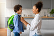 Happy black mother preparing child boy with backpack for school