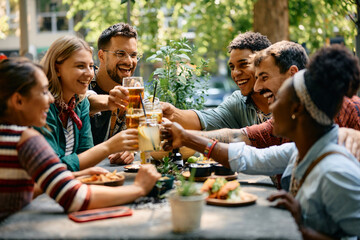 Wall Mural - Cheerful group of friends toasting while gathering for drink in cafe.