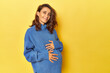 Pregnant woman caressing her belly on yellow