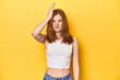 Redhead in white tank top, relaxed studio pose forgetting something, slapping forehead with palm and closing eyes.