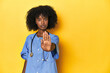 Young African-American nurse in studio with yellow background standing with outstretched hand showing stop sign, preventing you.