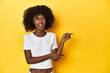 Teen girl in classic white T-shirt, yellow studio backdrop pointing with forefingers to a copy space, expressing excitement and desire.