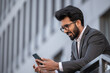 © zinkevych - Smiling good-looking hindu man texting on the phone and feeling contented