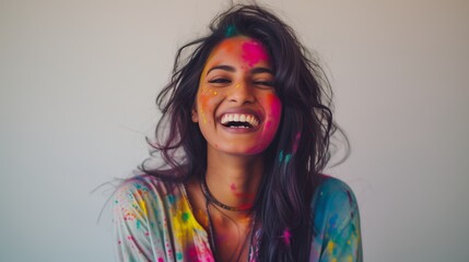 Exuberant young indian woman adorned with vibrant Holi colors laughing heartily against a light background