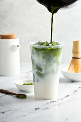 Wall Mural - Making iced matcha latte in a tall glass with ice by adding matcha tea to milk