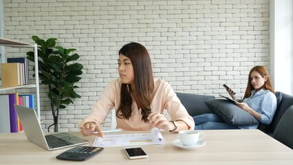 Wall Mural - Two asian Female freelance reading financial graph charts Planning analyzing marketing data. Asian people team working office firm. Two businesswomen team meeting using laptop at company office desk.