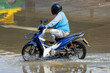 A taxi driver on a motorcycle drives through a flooded street
