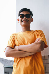 Young Asian teenage boy wearing sunglasses and standing with crossed arms outdoor