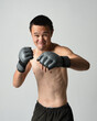 © faestock - Close up portrait of fit  asian male model, shirtless with muscles. Wearing gym shorthand boxing gloves, gestural punching pose. Isolated on a white studio background.
