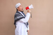 Asian muslim man in white robe with skullcap speaking louder using megaphone for advertisement
