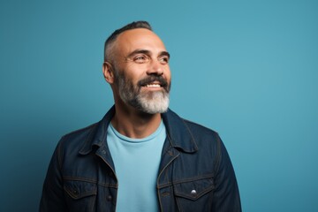 portrait of smiling mature man in denim jacket looking at camera over blue background