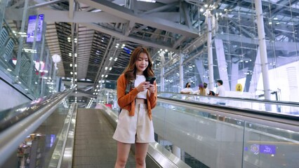 Wall Mural - Young asian woman in international airport terminal or modern train station. Backpacker passenger female commuter walking on escalator