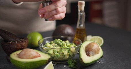 Wall Mural - Woman salting Chopped avocado in glass bowl at domestic kitchen