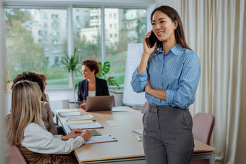 Businesswoman posing and talking on the phone while her colleagues work in the background