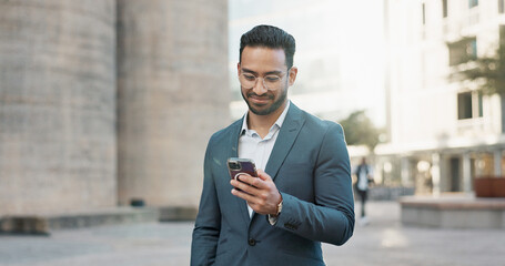 Canvas Print - Asian businessman, mobile message and walking in city, view and confident professional in career by office buildings. Young lawyer, chat and smartphone for connection and technology in cbd in town