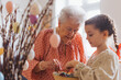 © Halfpoint - Grandmother with grandaughter decorating pussy willows branches, putting easter eggs on them.