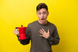 Young Brazilian man holding coffee pot isolated on yellow background surprised and shocked while looking right