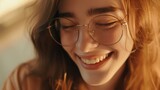 Fototapeta Panele - A young woman with glasses smiling gently her eyes closed with soft warm lighting and a blurred background that suggests a peaceful outdoor setting.
