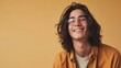 Young man with long hair and glasses smiling against a warm yellow background.