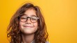 © iuricazac - A young girl with curly hair and glasses smiling against a bright yellow background.