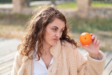 Young caucasian woman at outdoors holding an orange