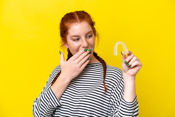 Young caucasian reddish woman holding invisible braces isolated on yellow background with surprise and shocked facial expression