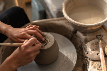 Close-up of a potter's hands expertly using tools to shape and detail a clay piece on the pottery wheel