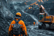 © Old Man Stocker - A mine worker in a soiled high-visibility jacket and safety helmet stands facing a large mining excavation site.
