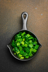 Wall Mural - Chopped spring onions in a sauce pan. On a dark background. Top view.