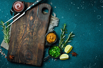 Sticker - Kitchen cutting board on table with spices, vegetables and herbs. Free space for a recipe. Rustic style. On a dark background.