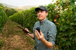 © scharfsinn86 - Farmer examines the vineyard and sends data to the cloud from the tablet. Smart farming and digital agriculture