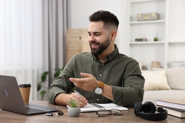 Poster - E-learning. Young man taking notes during online lesson at wooden table indoors