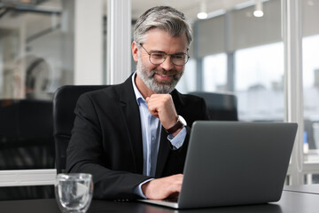 Canvas Print - Smiling man working with laptop at table in office. Lawyer, businessman, accountant or manager