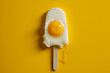 Popsicle made of sunny side up fried egg on vibrant yellow background. Creative food concept