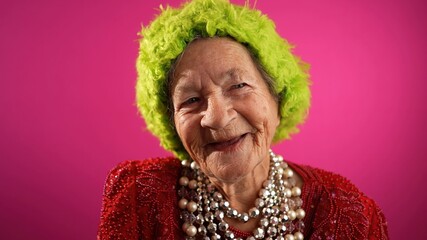 Closeup of laughing smiling elderly senior old woman with wrinkled skin and green wig on pink background.