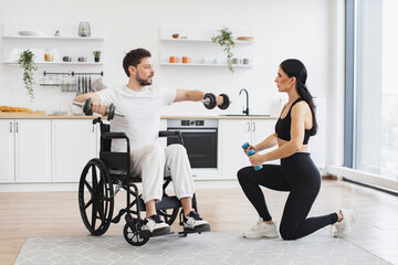 Female physiotherapist or wife showing mature male patient in wheelchair how to exercise with dumbbells at home. Rehab fitness for senior patients concept.