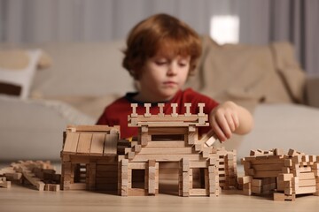 Poster - Cute little boy playing with wooden construction set at table in room, selective focus. Child's toy