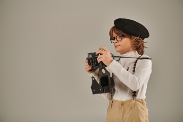 Wall Mural - cute boy, young photographer in beret and suspenders taking photo on retro camera in studio