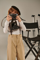 Wall Mural - boy in beret captures the moment on retro camera near director chair, young photographer in studio