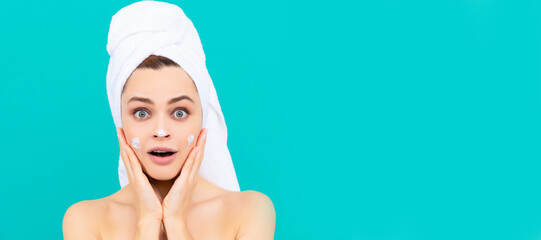 Poster - amazed young woman applying face cream on blue background. Beautiful woman isolated face portrait, banner with mock up copy space.