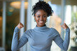 © Oliver Evans Studio - young black woman clenching fists showing off her muscles smiling student raising arms happy radiant face proud of her strength power success achievement victory cheerful indoors joyful earrings