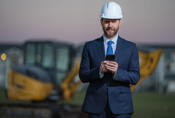 Wall Mural - Architect at a construction site. Architect man in helmet and suit at modern home building construction. Architect with a safety vest and suit. Confident architect standing at house background.