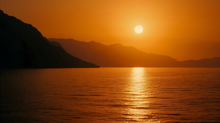 Sunset over the sea, with the sun dipping low in the sky, casting a warm orange glow over the calm sea and silhouetted mountains