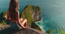Woman Enjoy Ocean Coastline Aerial Landscape Sit On The Rock Edge. Long Hair Brunette Tourist Girl Back View Relax Outdoor, Lifestyle Travel On Summer Holiday Vacation. Nusa Penida Island.