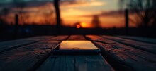 A Cell Phone Sitting On A Wooden Table At Sunset