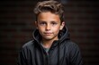 portrait of a boy in a black jacket against a brick wall