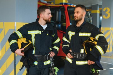 Wall Mural - Portrait of two young firemen in uniform standing inside the fire station