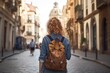 young female tourist with brown backpack from behind sightseeing in European city walking the street. Girl solo traveling in Europe, backpacking.